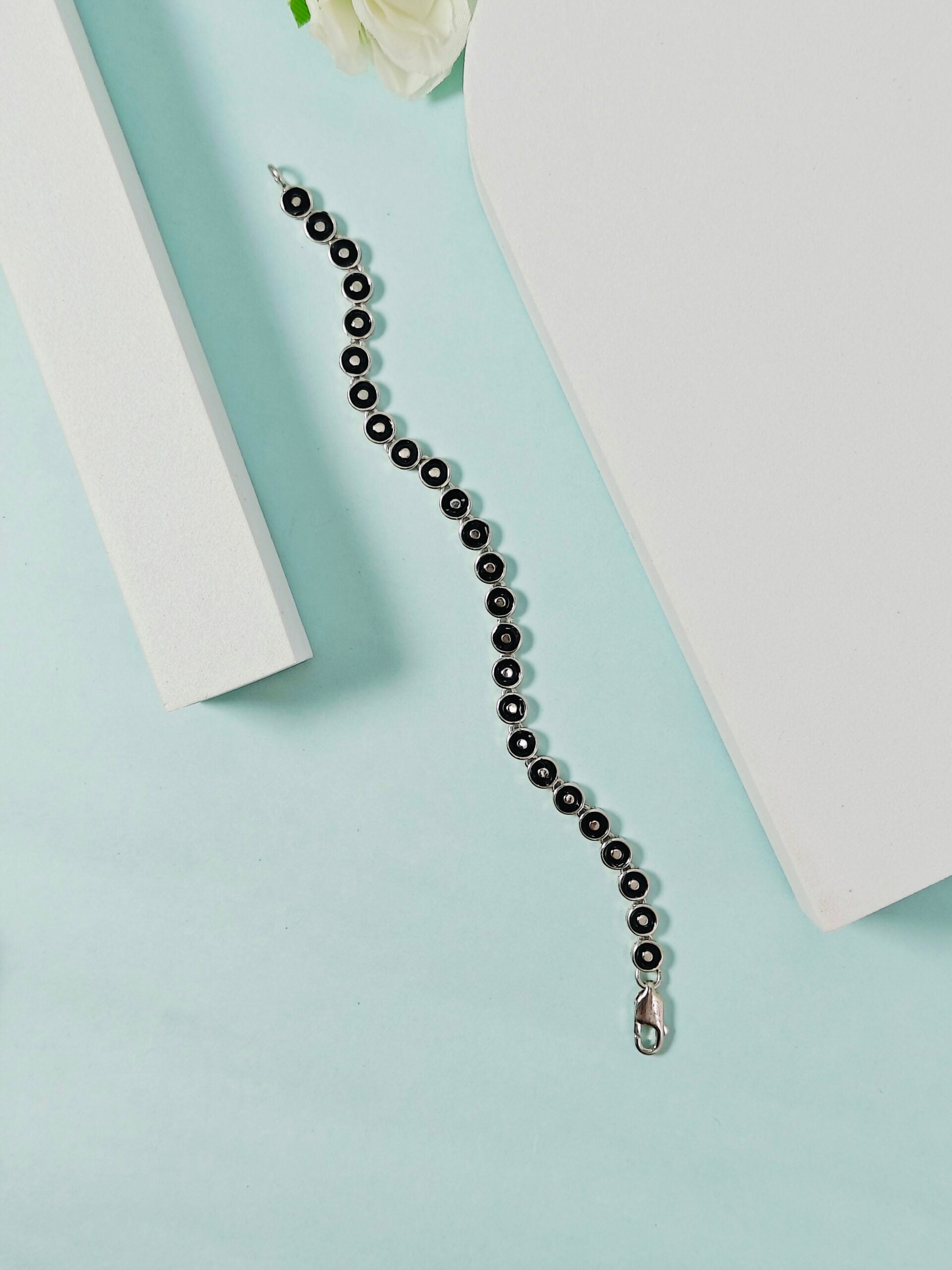 Black beaded necklace on a light blue surface with white flowers and books in the background